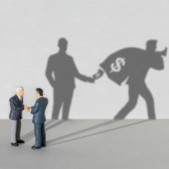 two business men shaking hands in the foreground while their shadows show one is stealing from the other.